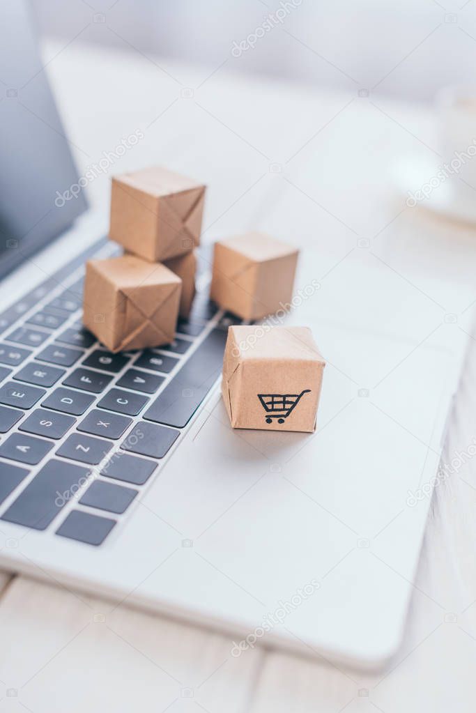 selective focus of toy paper boxes with shopping symbol on laptop keyboard 