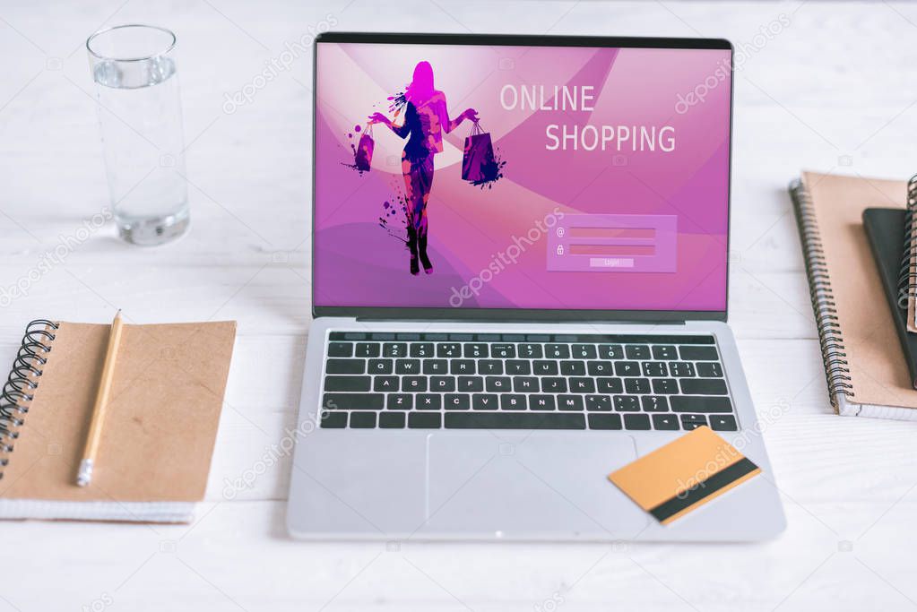 notebooks and laptop with shopping website on screen and credit card on wooden desk 