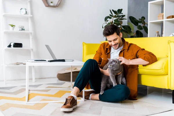 ブリティッシュショートヘアの猫と床に座ってハンサムな笑みを浮かべて男 — ストック写真