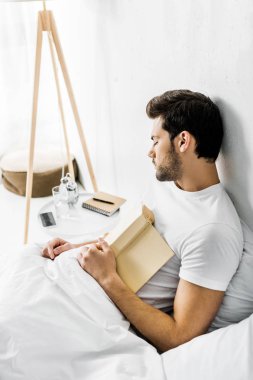 Genç adam yatakta uyurken defteri tutan 