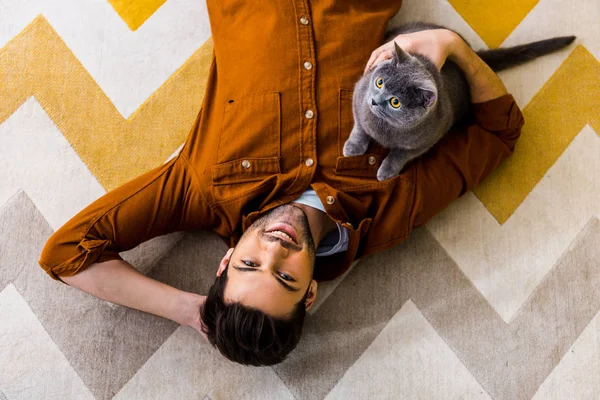 微笑的人躺在地毯上与英国速记猫的最高视图 — 图库照片