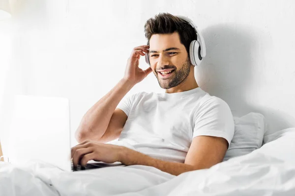 Cheerful Young Man Listening Music Headphones Laptop Bed — Stock Photo, Image