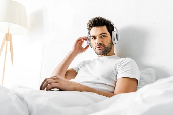 Όμορφος Άνδρας Ακούγοντας Μουσική Ακουστικά Και Laptop Στο Κρεβάτι — Φωτογραφία Αρχείου