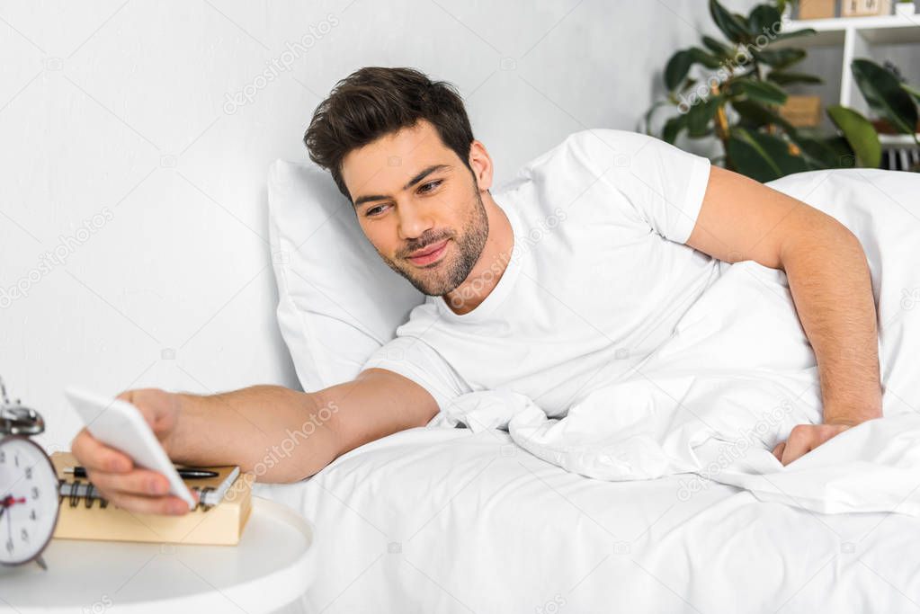 happy man waking up and looking at smartphone in the morning