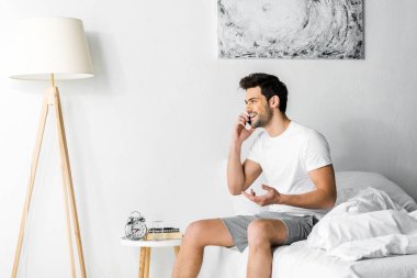 Sabahleyin yatakta otururken Smartphone'da konuşan yakışıklı gülümseyen adam