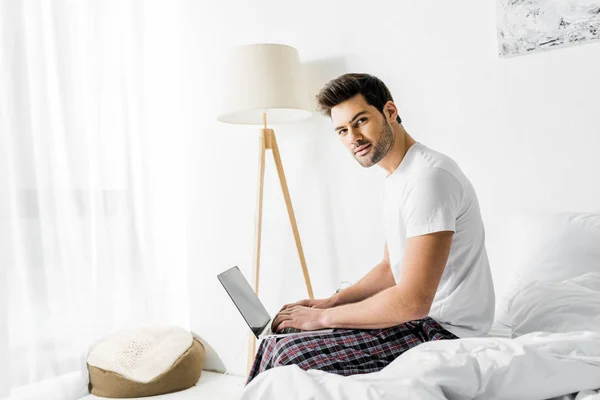 Przystojny Mężczyzna Pomocą Laptopa Siedząc Łóżku Rano — Zdjęcie stockowe