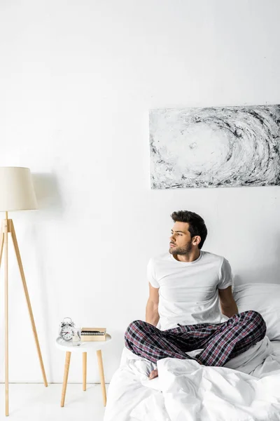 pensive man in pajamas sitting on bed in the morning