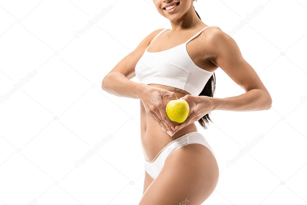 cropped shot of smiling young african american woman in underwear holding green apple isolated on white