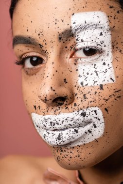 güzel Afrikalı-Amerikalı kadın kahverengi ve beyaz boya ile pembe üzerinde izole kamera bakıyor yüzüne su sıçramalarına