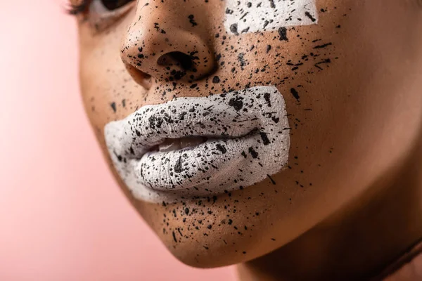 cropped shot of beautiful african american woman with white paint and brown splashes on face isolated on pink