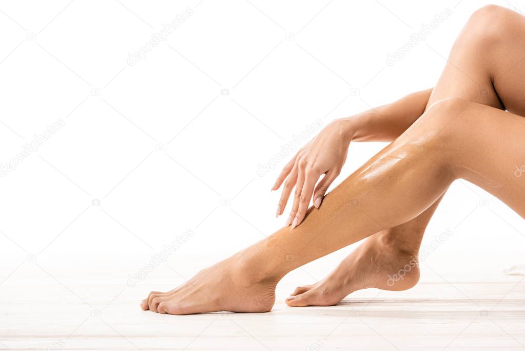 cropped shot of african american woman touching leg with sugar wax on white 