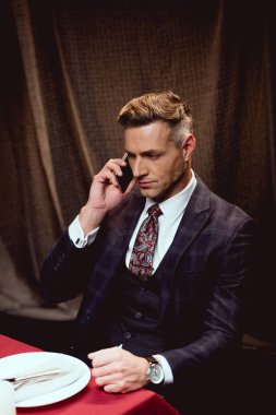 masada oturan ve restoranda Smartphone cep telefonu ile konuşurken elbiseli yakışıklı adam