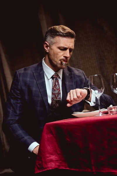 Dissatisfied Handsome Man Suit Sitting Table Smoking Cigar Looking Watch — Stock Photo, Image