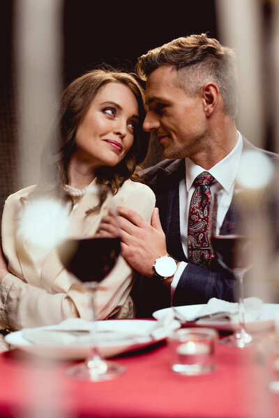 man embracing beautiful smiling woman during romantic date in restaurant