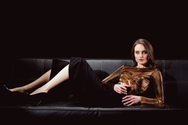 Kanepenin üstüne bir bardak kırmızı şarap ile yalan ve siyahta izole kamera bakıyor güzel zarif kadın