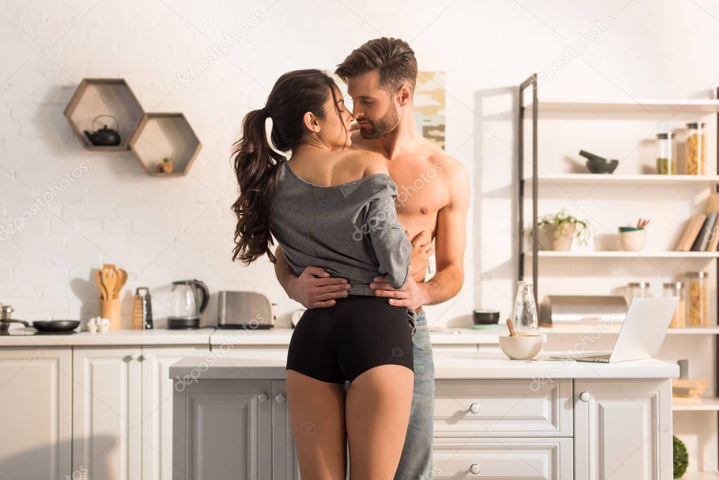 selective focus of young seductive couple passionately hugging in kitchen 