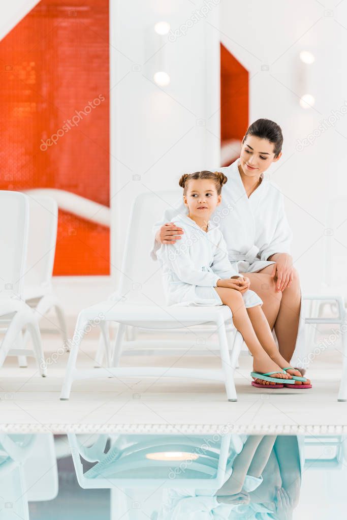 happy mother hugging daughter while sitting on deck chairs 