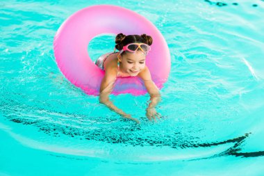 happy child learning swimming with inflatable ring in swimming pool clipart