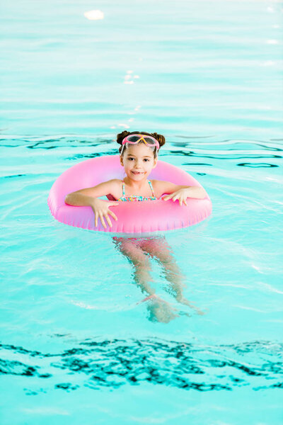 cheerful child learning swimming with inflatable ring in swimming pool