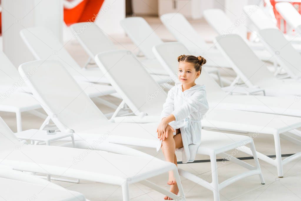 cute kid in white bathrobe sitting on deck chair 