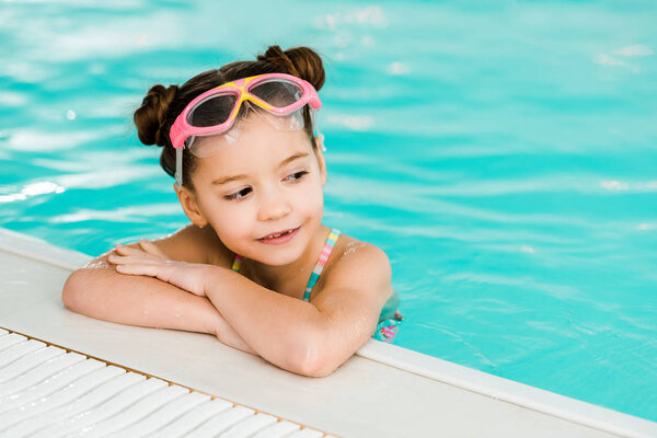 adorable child in googles swimming near poolside in swimming pool