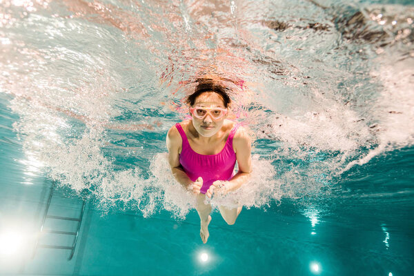 woman diving in googles underwater in swimming pool