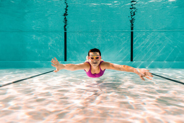 happy woman in googles diving underwater in swimming pool
