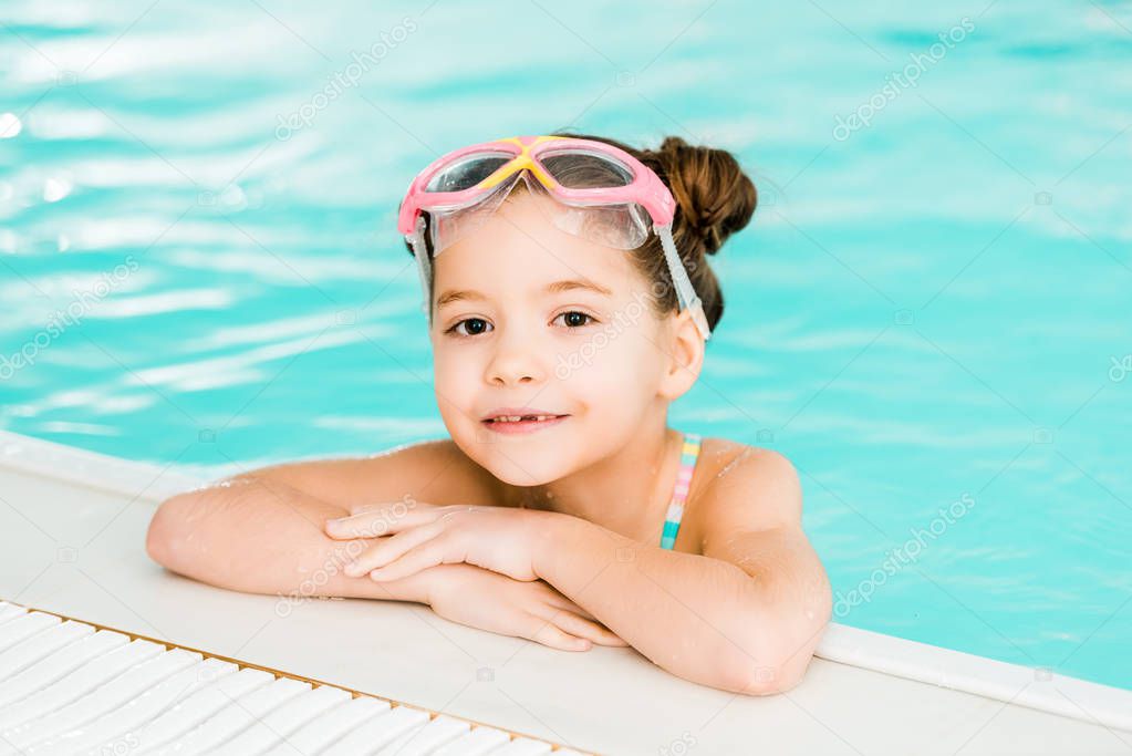 adorable kid in googles swimming near poolside in swimming pool