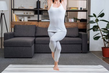 cropped view of woman practicing eagle pose at home in living room clipart