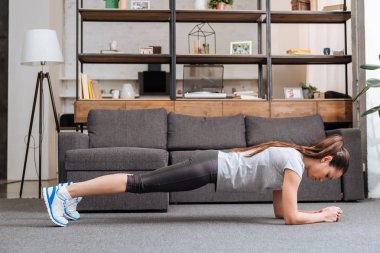 focused sportswoman doing plank exercise at home in living room