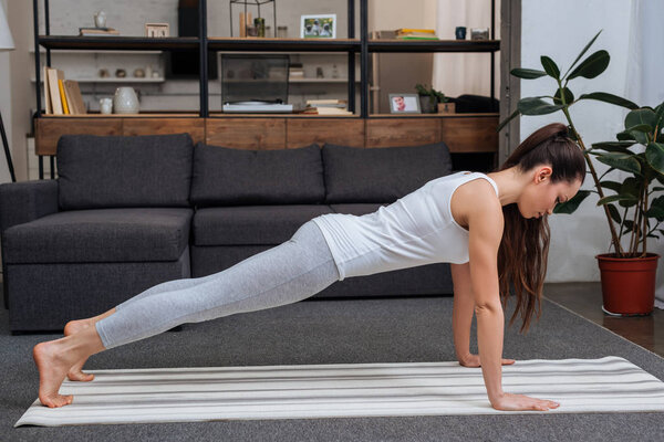 young woman practicing plank pose at home in living room