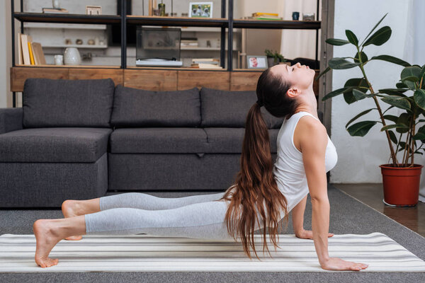 young woman practicing cobra pose in living room at home