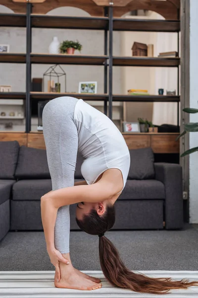 Ung Kvinna Tränar Stående Framåt Bend Pose Hemma Vardagsrummet — Stockfoto