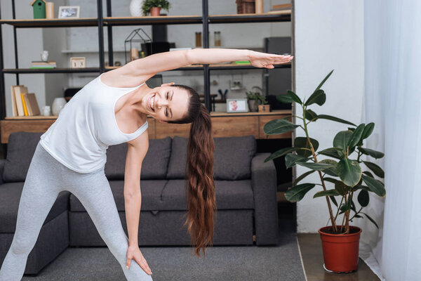 smiling young woman doing stretching exercise at home in living room