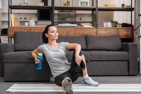 sportswoman with towel and sport bottle sitting in living room 