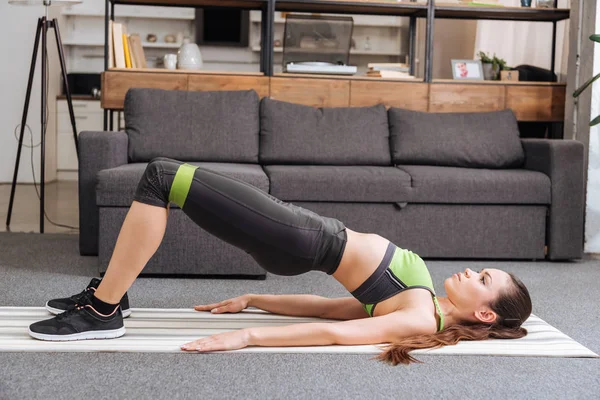 focused sportswoman training with resistance band at home in living room