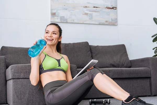 Χαμογελώντας Αθλήτρια Μπουκάλι Νερό Χρησιμοποιώντας Ψηφιακό Tablet Στο Σπίτι — Φωτογραφία Αρχείου