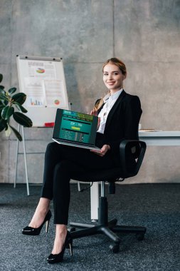 Businesswoman sitting in chair and holding laptop with football matches scores on screen clipart