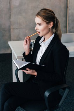 selective focus of beautiful businesswoman holding notebook and gnawing pencil clipart