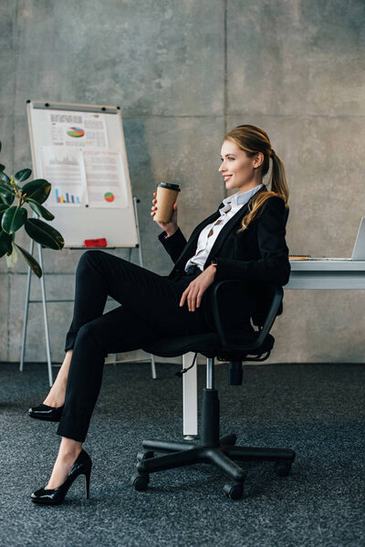 smiling businesswoman sitting on chair with paper cup of coffee