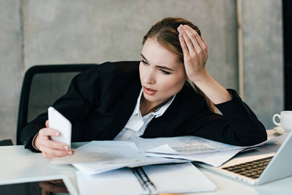 selective focus of beautiful businesswoman using smartphone and sitting at work-table