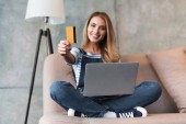 schöne Frau mit Laptop lächelt und zeigt Kreditkarte 