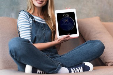 Kırpılan kanepe ve dünya dijital tablet ile gösteren ekran üzerinde oturan kız görünümünü