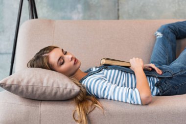 beautiful woman sleeping on pink sofa and holding book in hand
