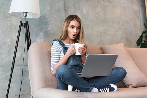 Conmocionado Joven Mujer Sosteniendo Taza Las Manos Sentado Con Ordenador —  Fotos de Stock