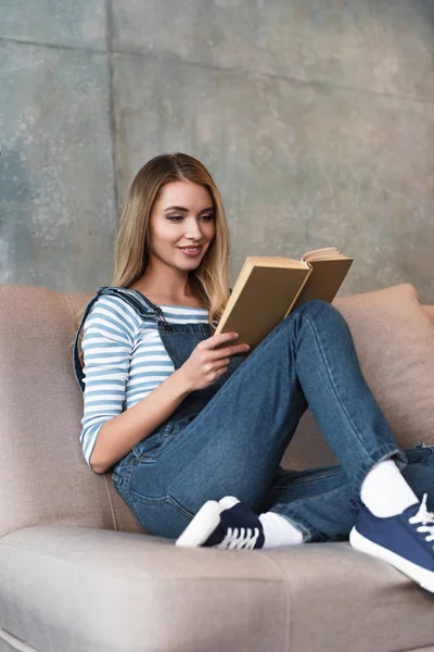 Jovem Sorrindo Menina Sentada Sofá Rosa Livro Leitura — Fotografia de Stock