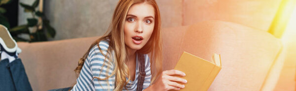shocked young woman in room with sunshine holding book in hands