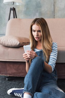 Smartphone kullanarak ve pembe kanepe oturan genç kadın