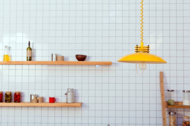 wooden shelves, jars and lamp in kitchen with white tile on background