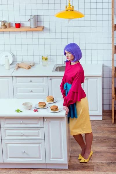 紫髪とパンケーキとキッチン カウンターに近いポーズのカラフルな服を持つ主婦 — ストック写真